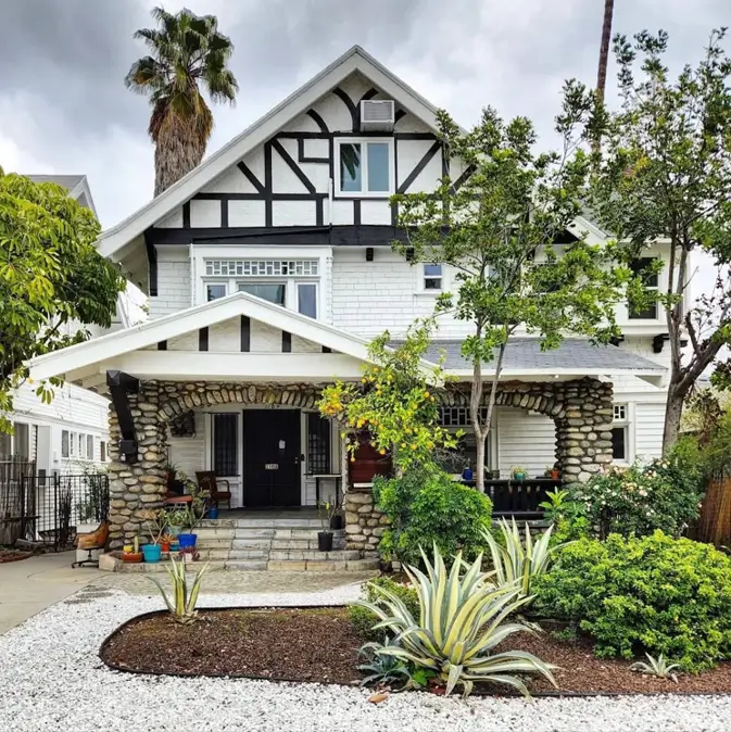 A white craftsman house exterior with Tudor-style half-timbering, an arched porch, and large river rock columns.
