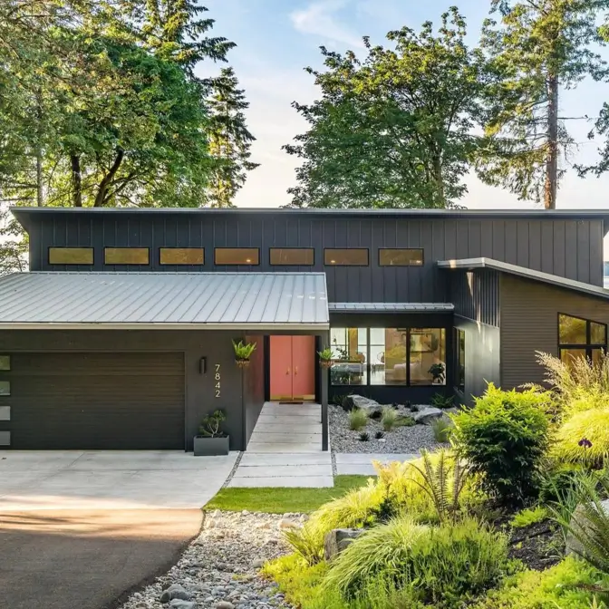 A dark modern house with low-slung, mid-century modern rooflines and a row of clerestory windows.