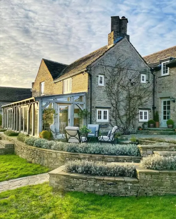 A stone British country house with a terraced patio and a modern glass conservatory.