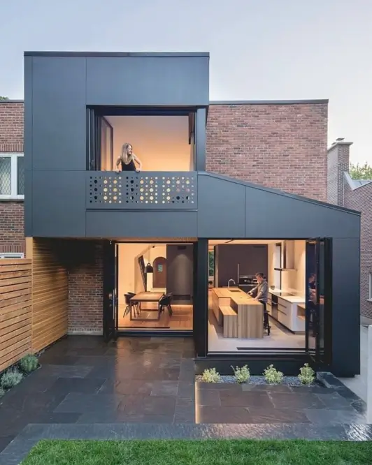 A modern black-clad extension with large glass doors contrasting with the original brick of an older home.