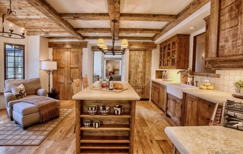 An open-concept rustic kitchen design featuring heavy wood beams, a comfortable seating area, and matching wood cabinetry.