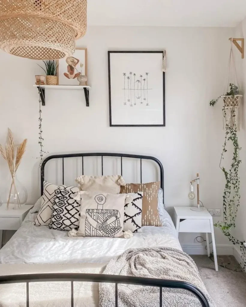 A bright boho bedroom with a black metal bed, featuring a framed palm tree line art print and a macrame plant hanger on the wall.