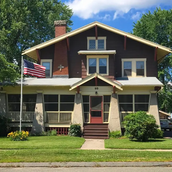 A dark brown craftsman house exterior with a large screened-in porch and massive tapered stucco columns.