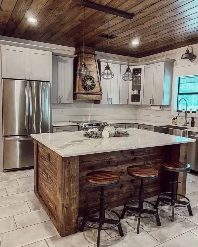 A modern rustic kitchen with a dark wood-clad ceiling, a reclaimed wood island, and light grey shaker cabinets.