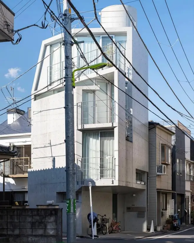 A tall, narrow contemporary concrete home with stacked balconies, designed for a compact urban lot.