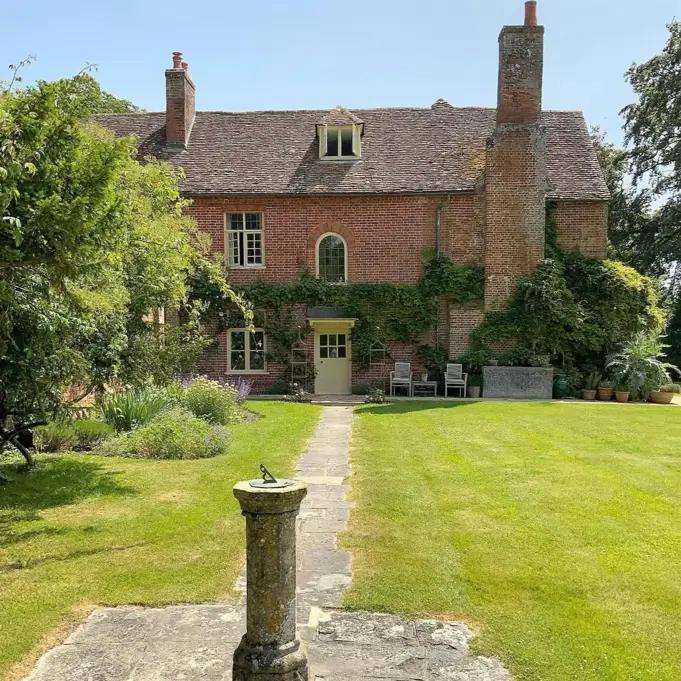 A red brick English country house with a large lawn and a classic stone sundial in the foreground.