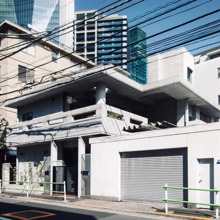 A low-profile modern concrete home with a large overhanging roof, set against a backdrop of city skyscrapers.