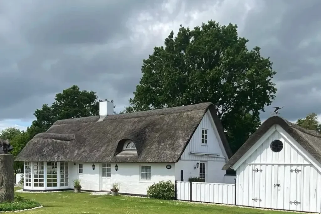A classic country house design featuring a white cottage with a traditional thatched roof and a matching outbuilding.