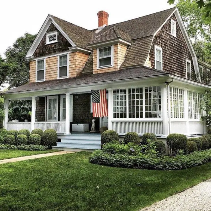 A classic country house design featuring a welcoming wraparound porch and natural cedar shingle siding.