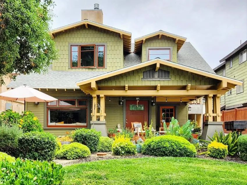 A craftsman house exterior painted in warm olive green with golden-tan trim, a red front door, and a large covered porch.