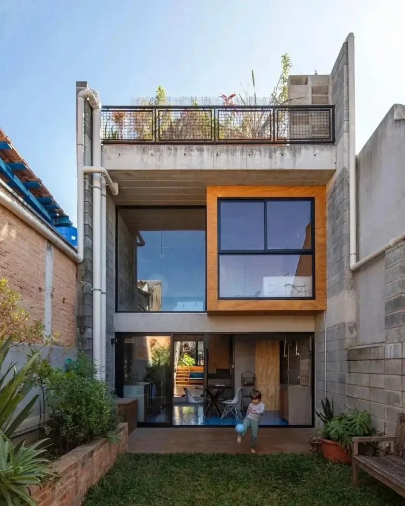 The back of a narrow modern concrete home with a full glass wall and a rooftop garden.