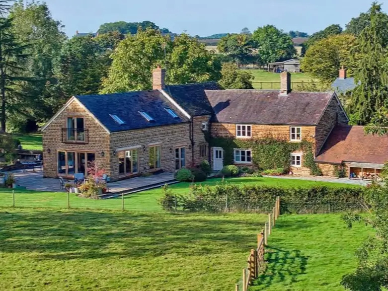 A classic stone country house design with a modern addition that opens onto a stone patio overlooking green fields.