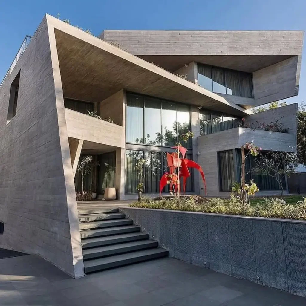 A modern concrete home with dramatic angular architecture and a large red sculpture in the front garden.