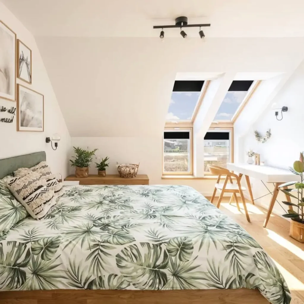 A sunlit attic bedroom featuring a bed with a bold green monstera leaf print duvet and skylight windows.