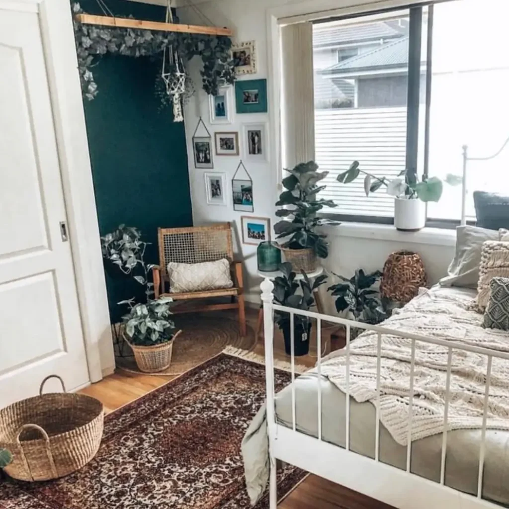 A cozy bedroom corner with a dark accent wall, a rattan chair, and a small gallery wall next to a bed.