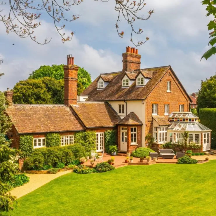 A grand brick country house design featuring a glass conservatory that opens onto a pristine lawn and patio.