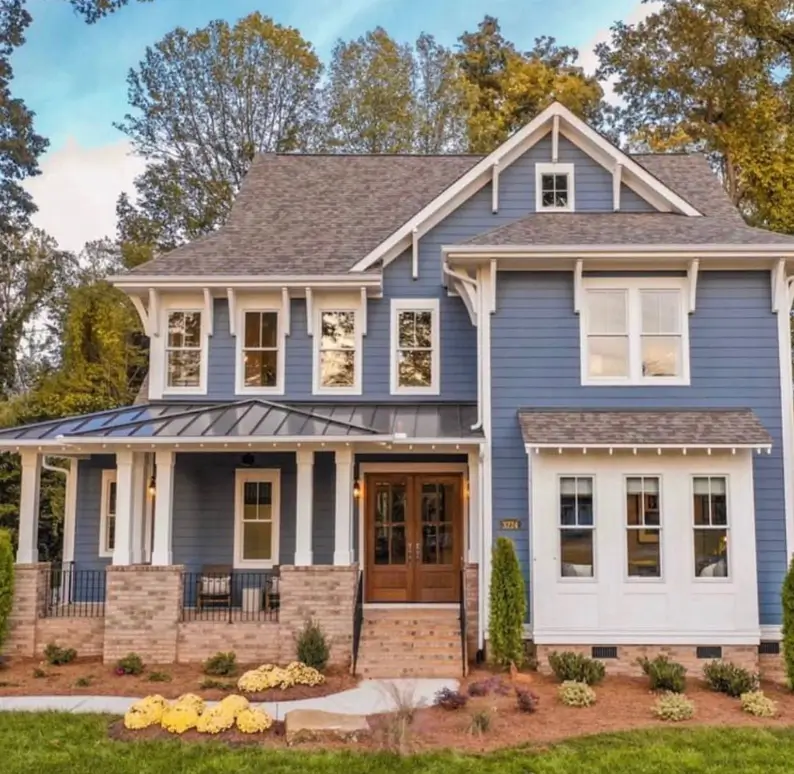 A craftsman house exterior in dusty blue with white trim, a front porch with brick piers, and double wood entry doors.