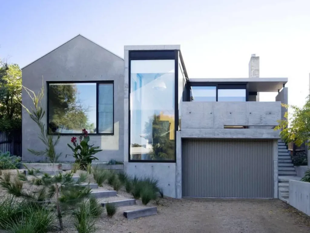 A modern concrete house with a mix of geometric shapes, including a gabled roof and a glass-fronted central cube.