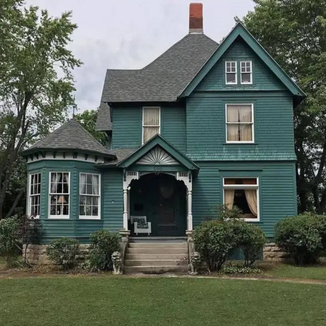 A historic country house design with deep teal siding, a corner turret, and intricate white porch details.