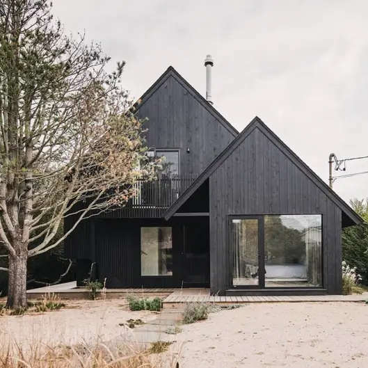 A modern black A-frame house with clean geometric lines, nestled in a minimalist, natural setting.