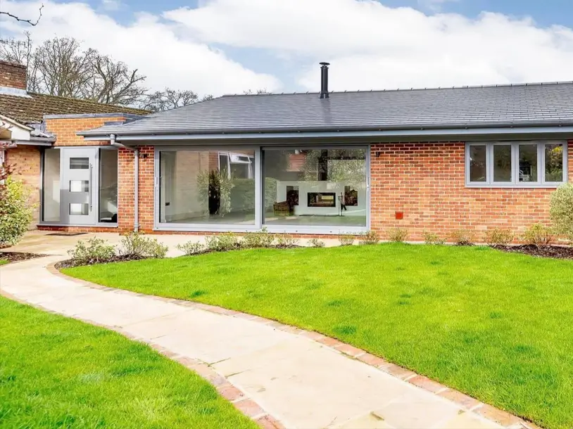 A modernized red brick ranch house featuring a large picture window with dark gray frames.
