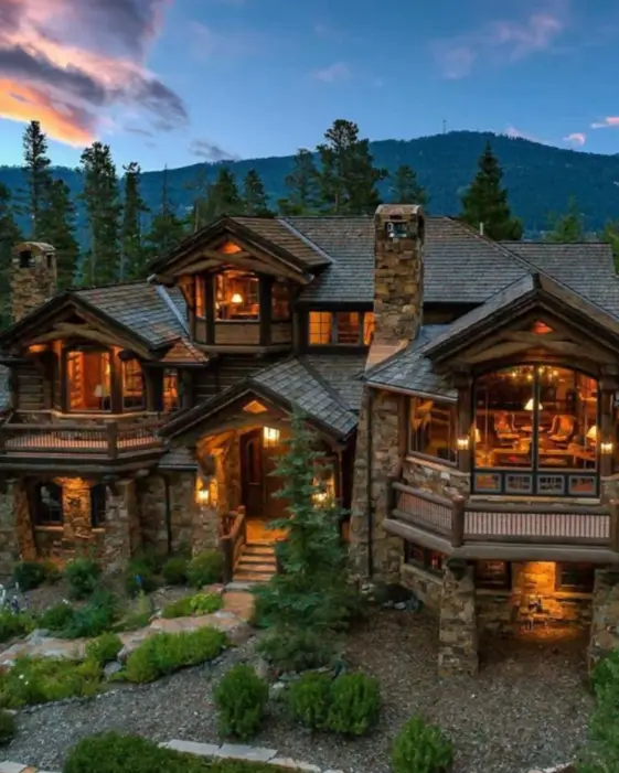 16 Mountain Mansions That Define Luxury Alpine Living 8 A welcoming luxury mountain mansion at twilight, with strategic lighting creating a warm, inviting glow from its stone and timber structure.