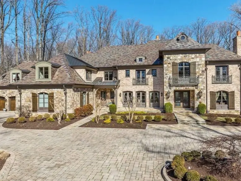20 Stone Mansion Ideas for Classic & Modern Designs 6 A sprawling stone and brick mansion featuring wrought-iron Juliet balconies, wooden shutters, and a large paver stone motor court.
