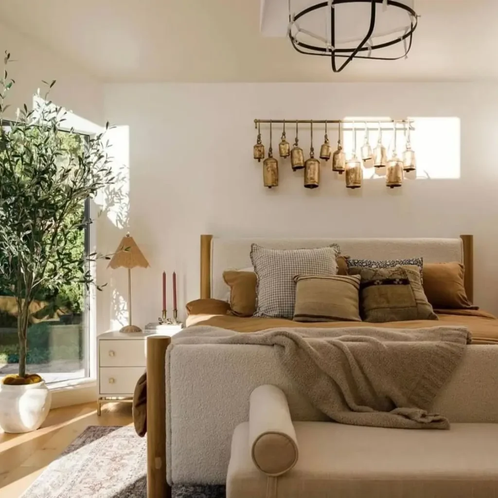 A sunlit, sophisticated bedroom with a cream bouclé bed frame, layered with warm-toned pillows and a knit throw.