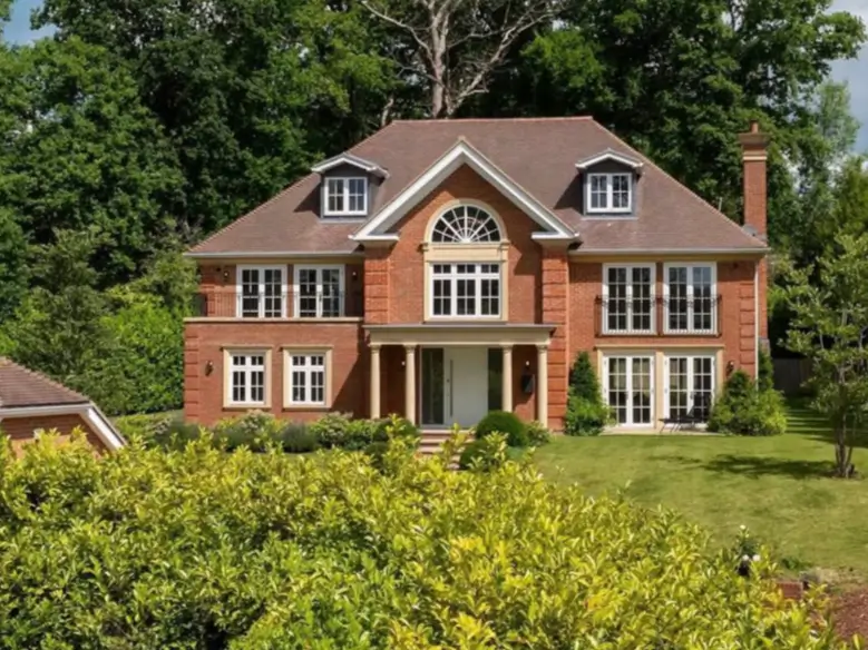 A grand modern country house design featuring a red brick exterior, a large arched window, and symmetrical Juliet balconies.