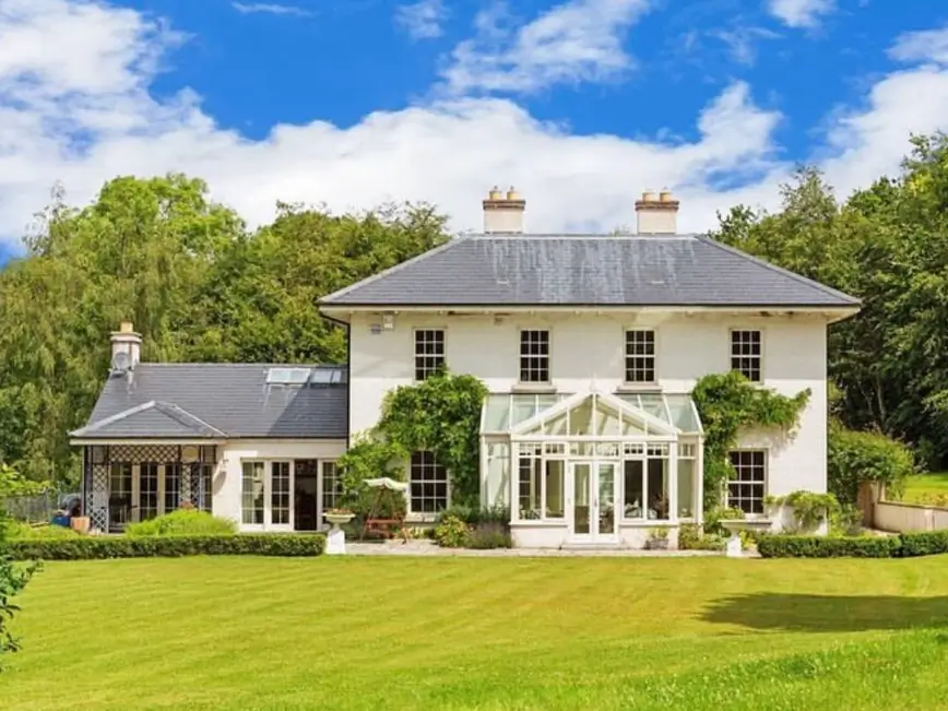 An elegant country house design with a pristine, expansive lawn and a central glass conservatory.