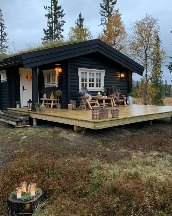 60 Charming Small Log Cabin Ideas to Inspire Your Rustic Retreat 43 A modern black small log cabin with a large wooden deck and a green living roof at dusk.
