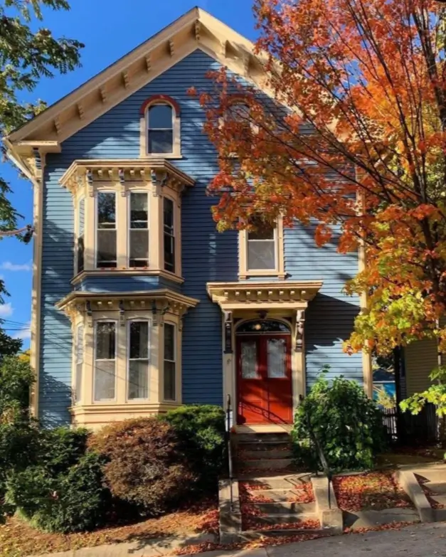 A colorful country house design featuring blue siding, cream trim, a bright red door, and bay windows.