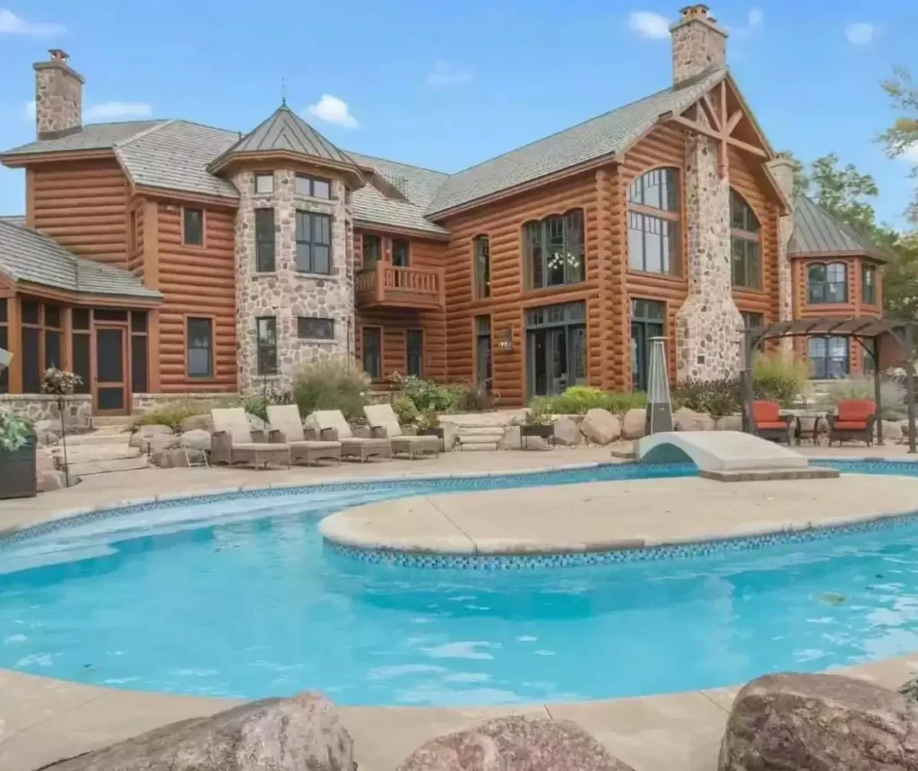 Embracing Grandeur: 25 Inspiring Ideas for Large Log Cabin Homes 8 A large log cabin home with a stone turret overlooking a custom swimming pool and patio with lounge chairs.