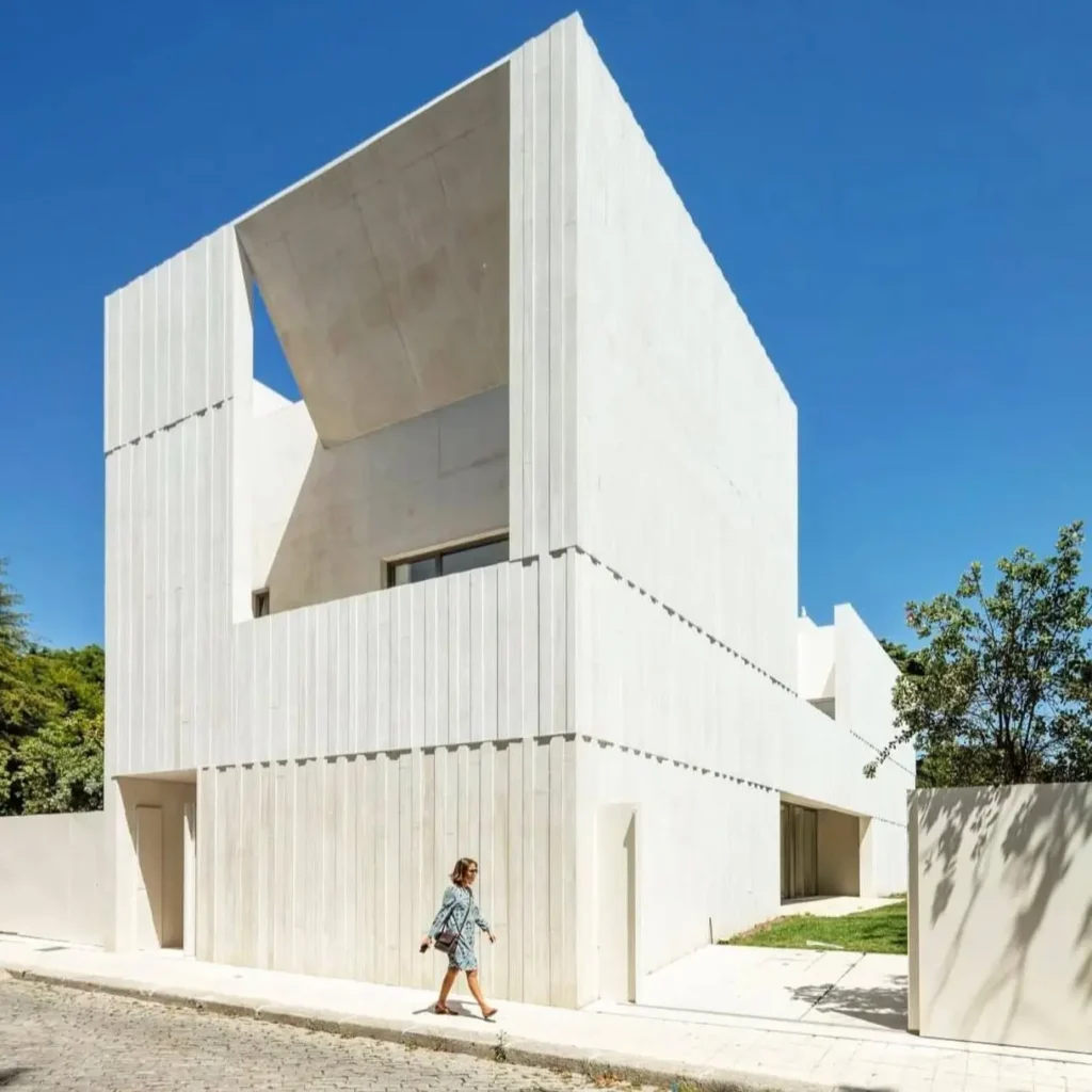 A striking modern concrete house with a fluted white exterior and deep-set windows under a clear blue sky.