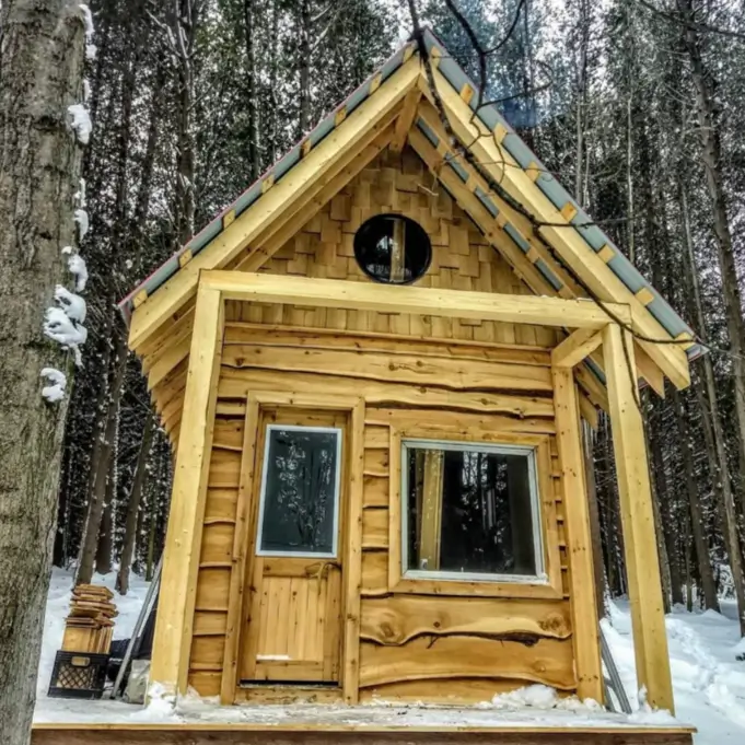 60 Charming Small Log Cabin Ideas to Inspire Your Rustic Retreat 7 A small, rustic wooden cabin in the snow featuring a round window and a steep roof.