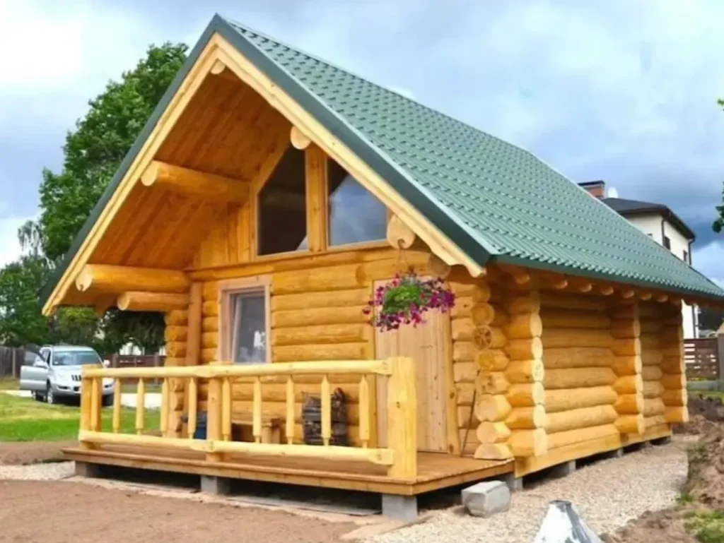 60 Charming Small Log Cabin Ideas to Inspire Your Rustic Retreat 52 A light-colored small log cabin with a green metal roof and a large triangular window in the gable.