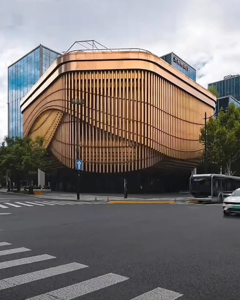 A modern building featuring a kinetic facade of moving bronze tubes that create a fluid, wave-like pattern.
