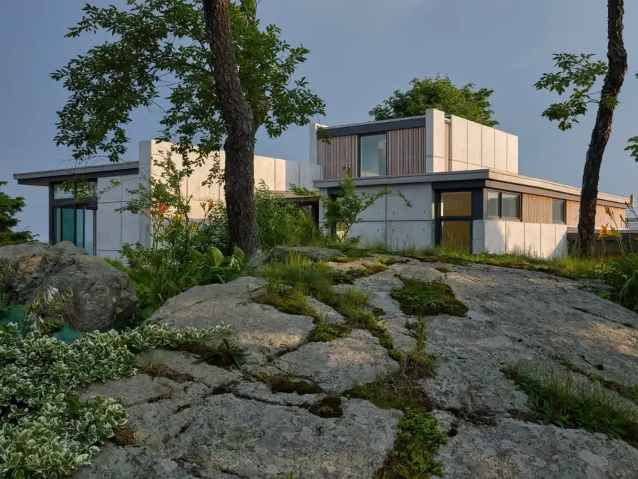 A modern concrete home with wood accents built into a rocky, tree-filled landscape.