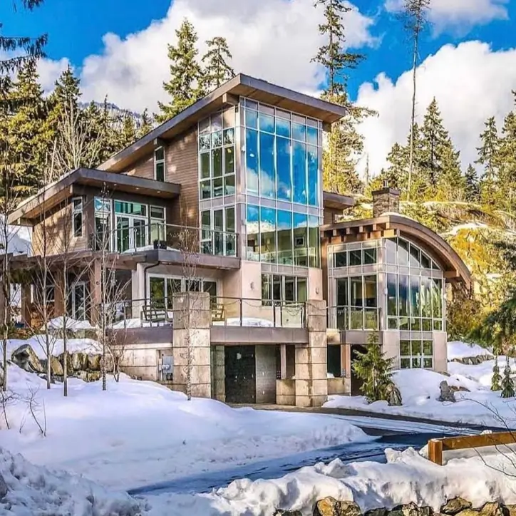 16 Mountain Mansions That Define Luxury Alpine Living 10 A modern mountain mansion featuring a two-story wall of windows that perfectly captures the vast, snow-covered landscape.