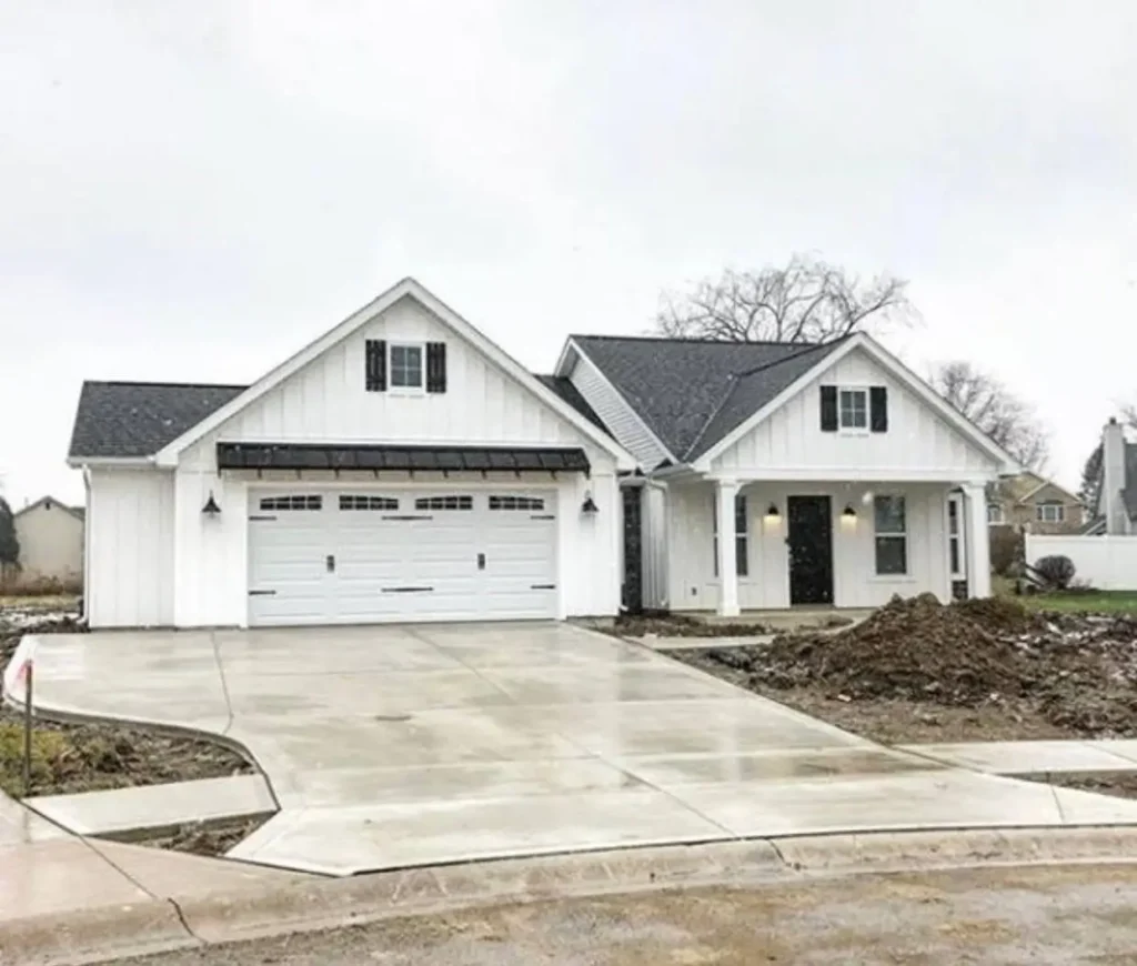 A new white modern farmhouse ranch with a black roof, shutters, and a metal garage awning.