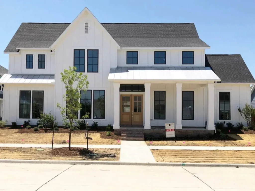 An off-white modern farmhouse with a prominent gabled entrance, thick white columns, and a light wood double front door.