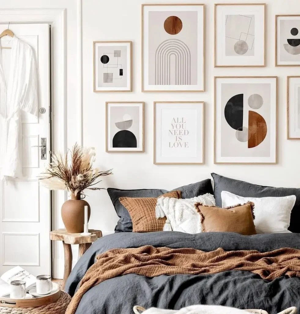 A modern boho bedroom with a large gallery wall of abstract geometric art in light wood frames above a bed with charcoal and rust linens.