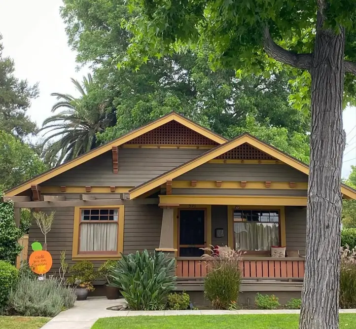 A craftsman bungalow with earthy brown siding and golden-yellow trim on the gables and a front porch.