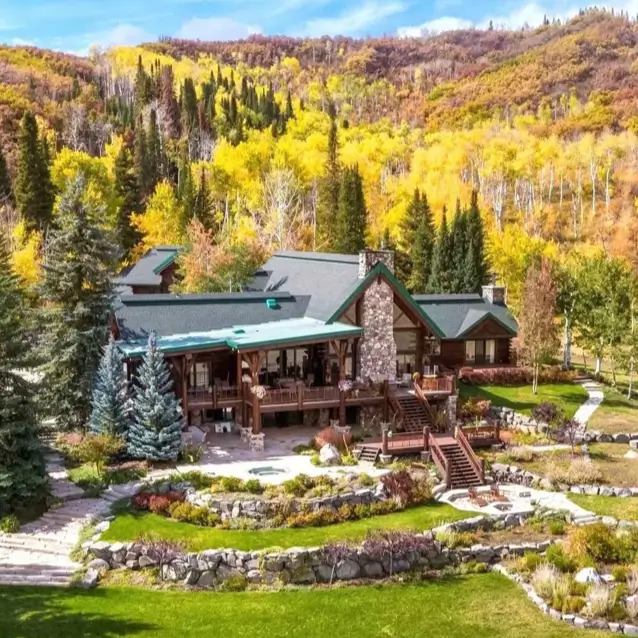 Embracing Grandeur: 25 Inspiring Ideas for Large Log Cabin Homes 10 A sprawling log cabin home with terraced stone landscaping and covered porch, set against a vibrant autumn forest.