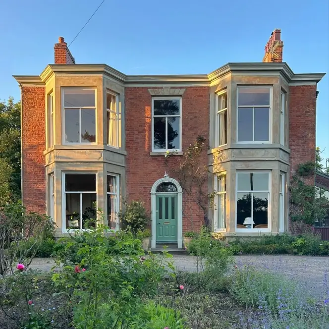 A red brick British country house with prominent two-story bay windows and a green front door.