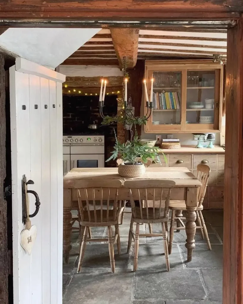 A simple rustic kitchen featuring a wooden dining set, stone flooring, and an antique-style candelabra light fixture.