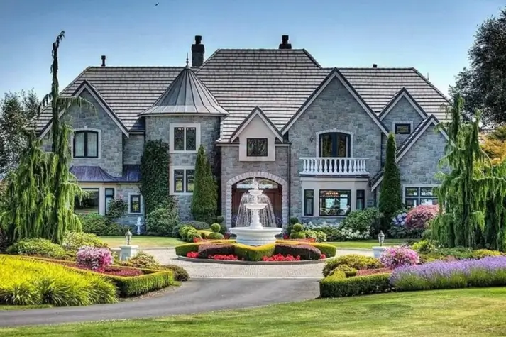 20 Stone Mansion Ideas for Classic & Modern Designs 9 A classic stone mansion featuring a circular driveway and a prominent white fountain surrounded by immaculate, colorful gardens.