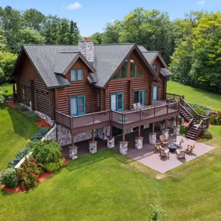 Embracing Grandeur: 25 Inspiring Ideas for Large Log Cabin Homes 11 An aerial view of a big log cabin featuring a walkout basement, a large upper deck with stone pillars, and a lower patio.