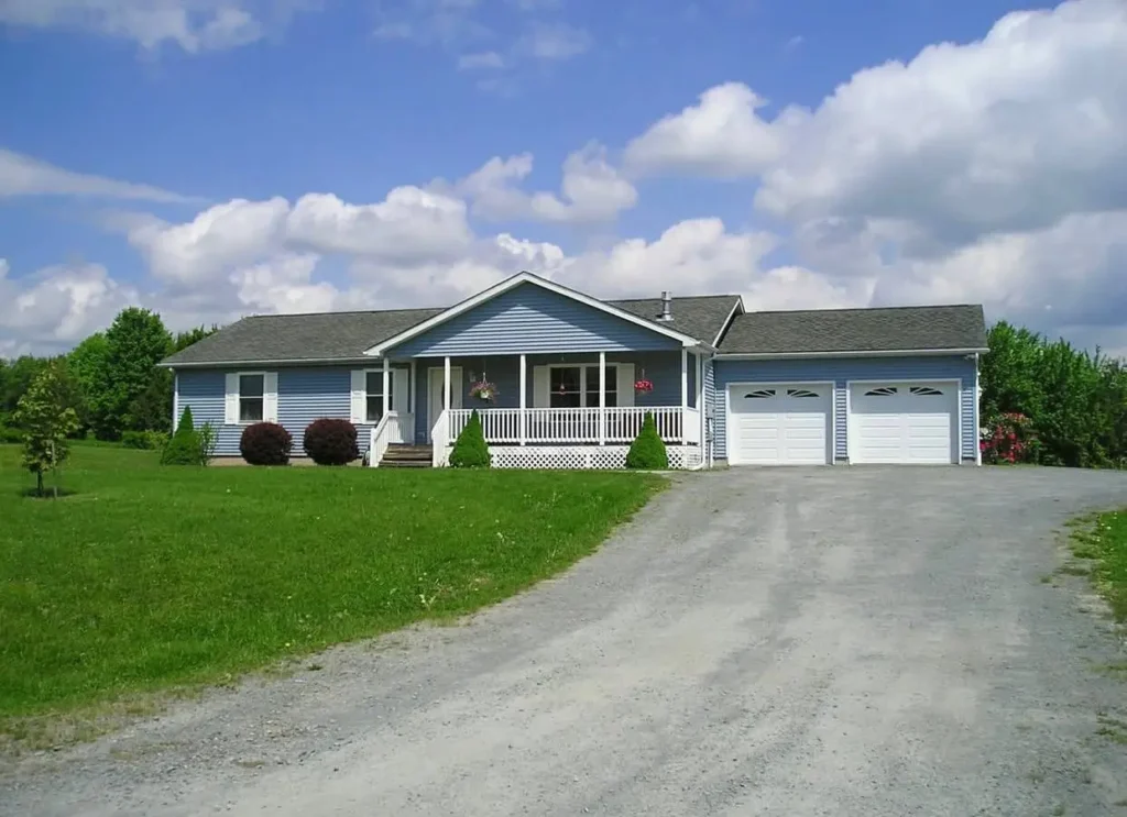 A classic blue ranch house with a white covered front porch and an attached garage on a sunny day.