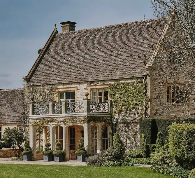 Stone British country house exterior with an ornate iron balcony and climbing ivy on the wall.